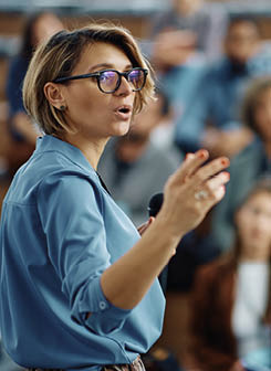 Mid adult businesswoman talking to group of seminar attendees in conference hall.
