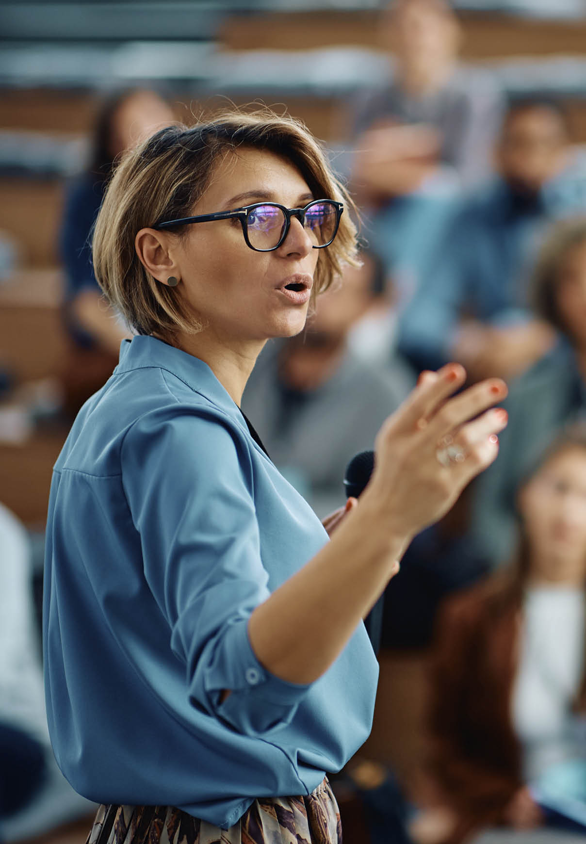 Mid adult businesswoman talking to group of seminar attendees in conference hall.