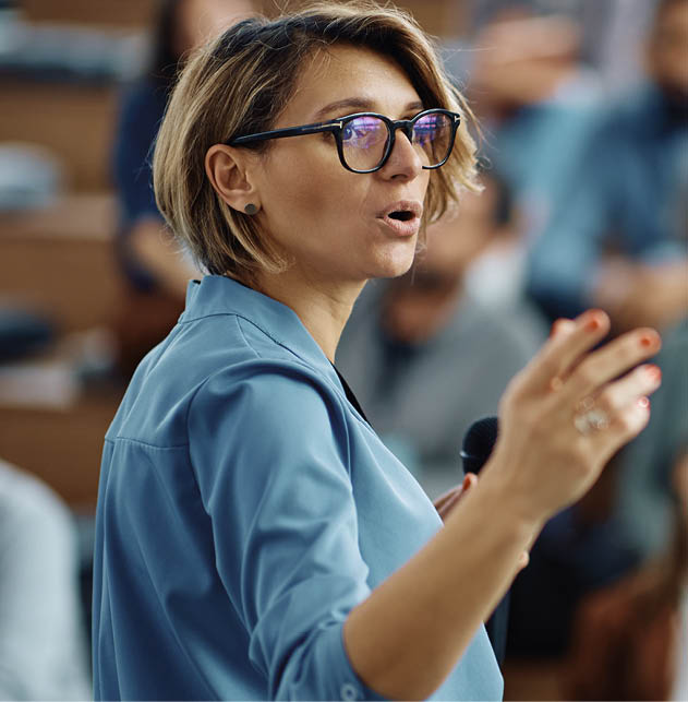 Mid adult businesswoman talking to group of seminar attendees in conference hall.